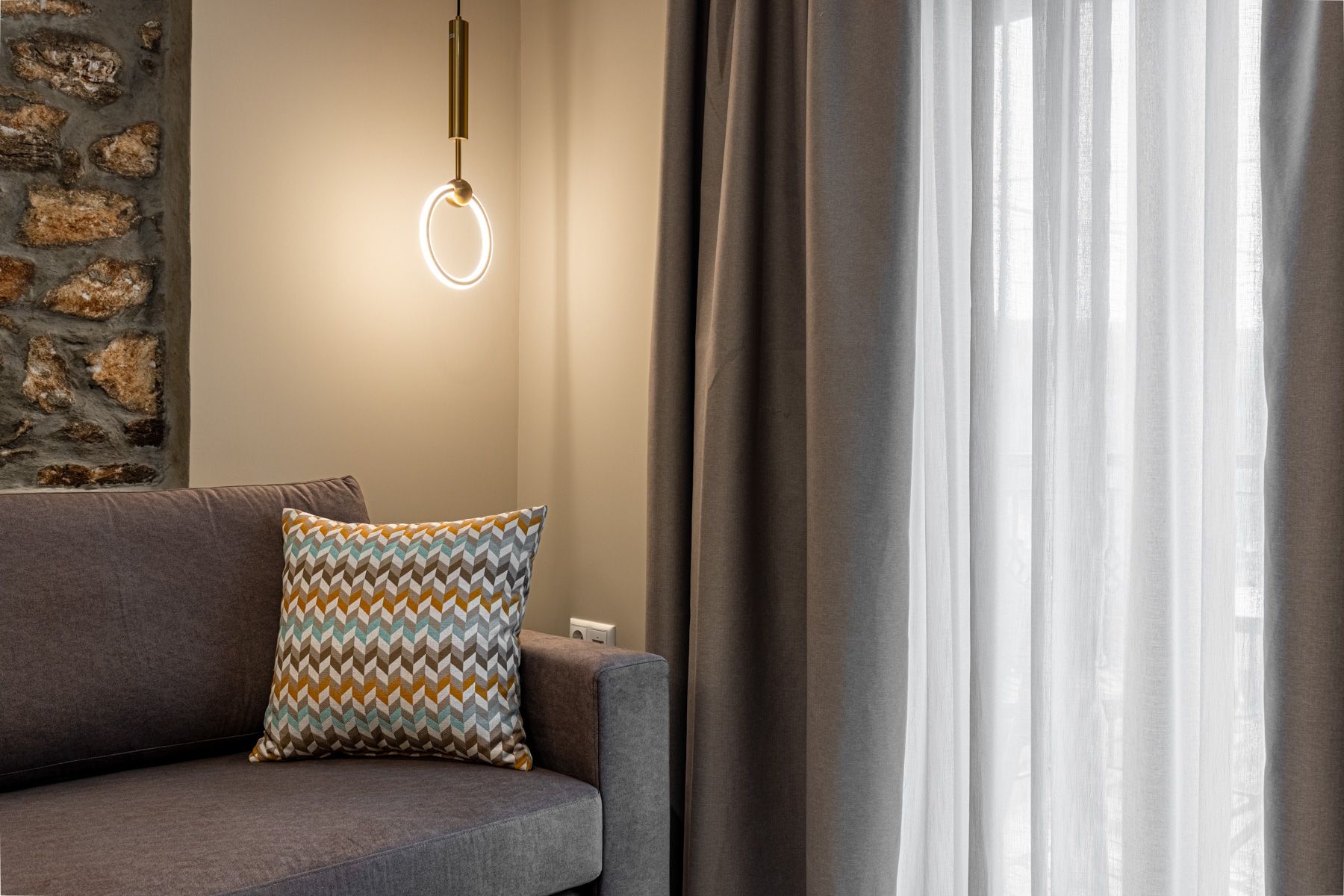 A woven cushion on the sofa in Asteroessa, lit by a brass ring pendant