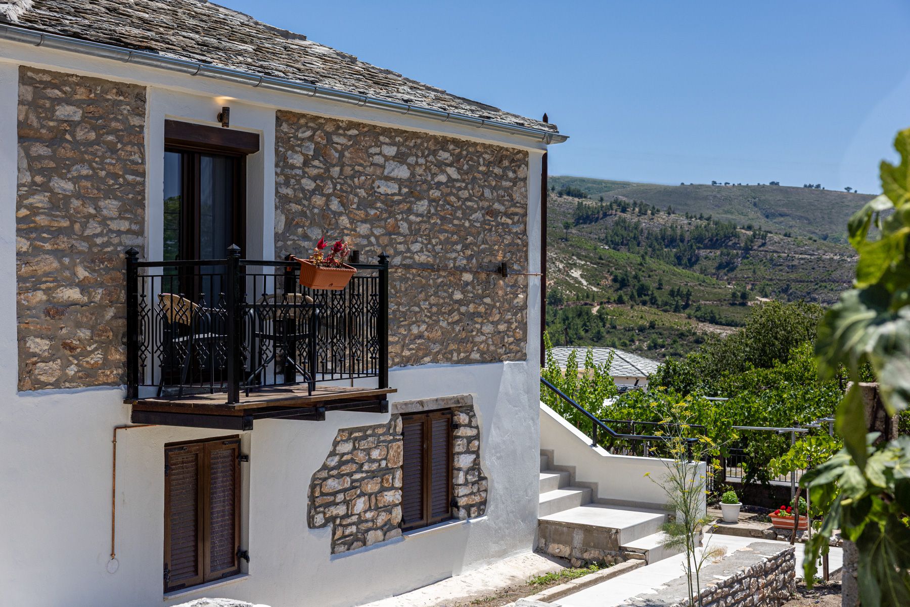 The stone facade from the side, iron balcony above the vines